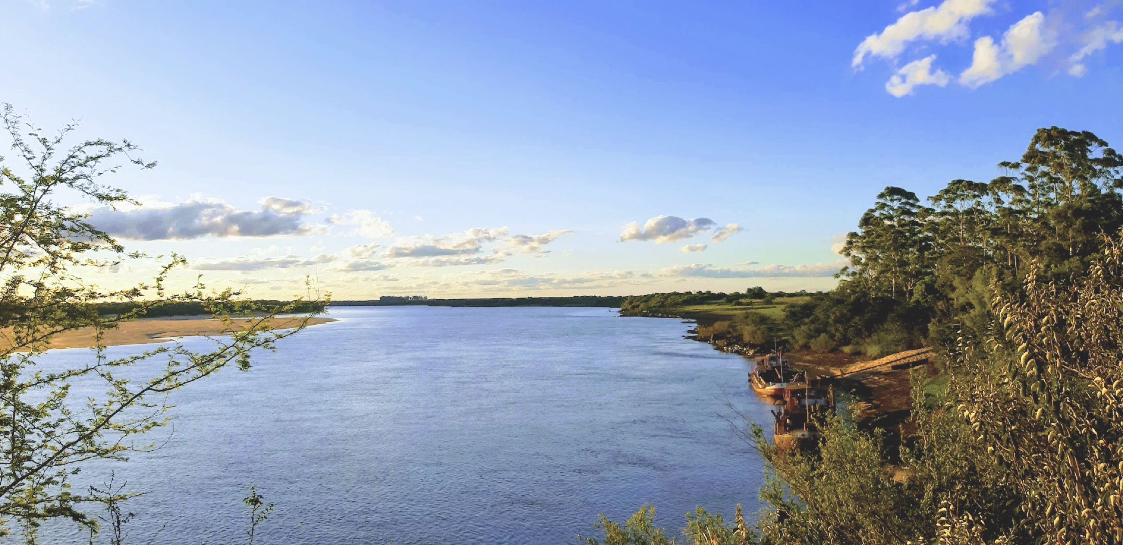 Rio amplo sob céu azul claro, emoldurado por vegetação verde